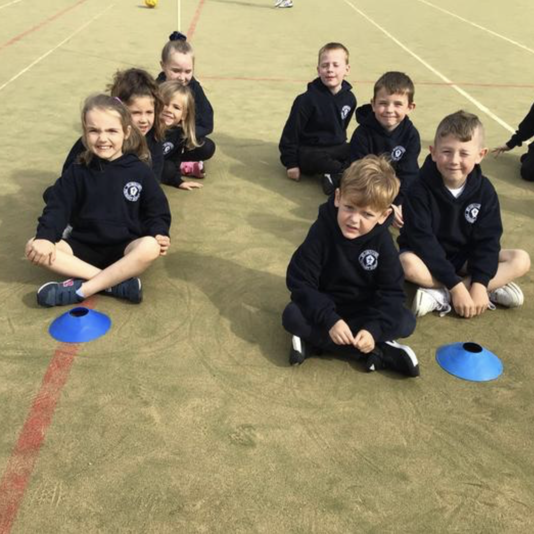 A group of boys and girls are sat in two lines during a PE lesson